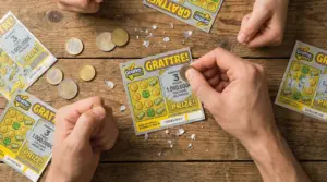 Mani che grattano biglietti Gratta e Vinci su un tavolo di legno con monete sparse