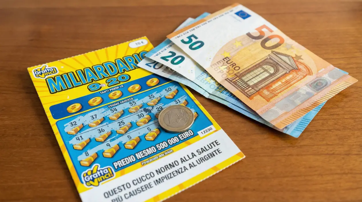 Biglietto del gratta e vinci con moneta da un euro e banconote su un tavolo