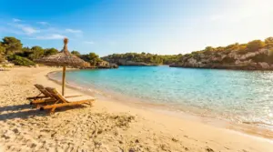 Spiaggia tranquilla con sabbia dorata, mare turchese e due lettini sotto un ombrellone di paglia