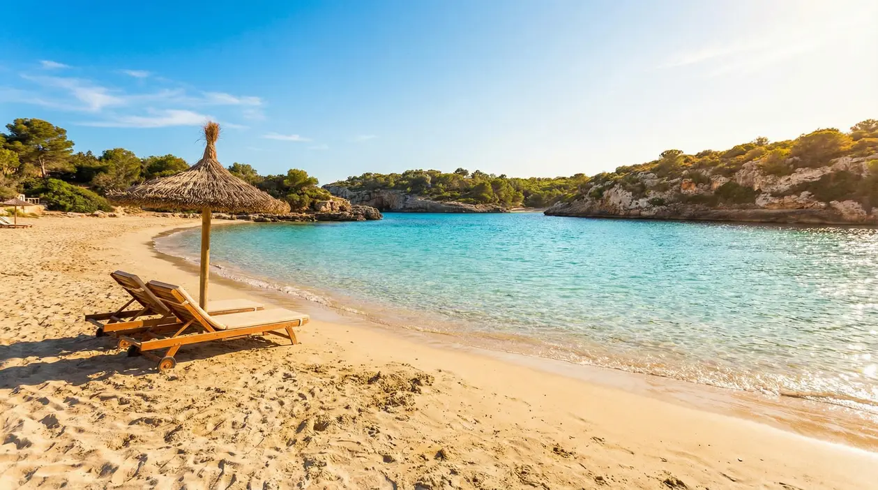 Spiaggia tranquilla con sabbia dorata, mare turchese e due lettini sotto un ombrellone di paglia