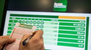 Una persona compila una schedina del Superenalotto davanti a uno schermo con i risultati